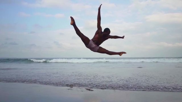 Contemporary ballet dancer performing at the beach. Gimbal shot on young attractive and athletic black African American man dancing by the sea