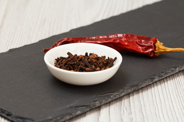 Cloves in a bowl and dry red pepper on stone cutting board