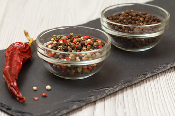 Allspice berries in bowls and dry red pepper on stone cutting board.
