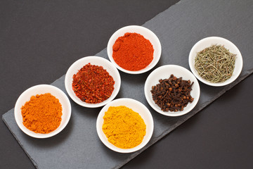 Various ground spices and herbs on stone cutting board.