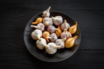 Onions and garlic on a black plate on a dark wooden old background.