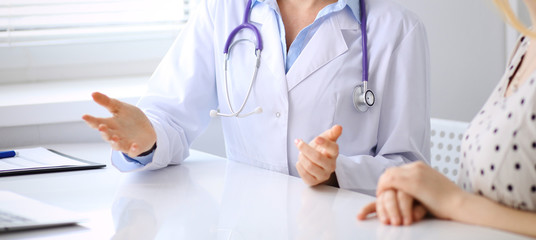 Doctor and patient discussing something while sitting at the desk at hospital, close-up. Medicine and health care