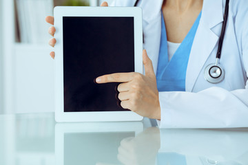 Female doctor using tablet computer while sitting at the workplace, close-up of hands. Medicine, healthcare and help concept