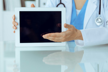 Female doctor using tablet computer while sitting at the workplace, close-up of hands. Medicine, healthcare and help concept