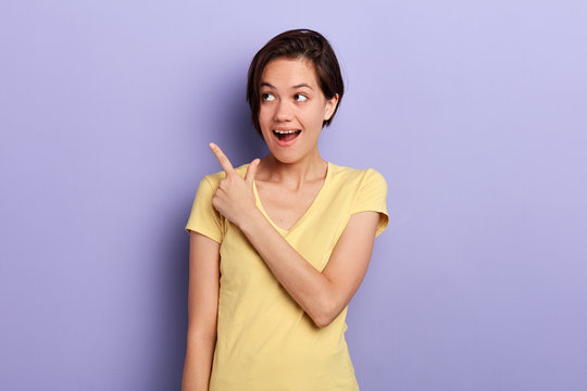 Joyful adorable bruette happy woman pointing up with her finger. look here. isolated blue background, studio shot. sale, discount, shopping, advert , place for text