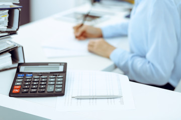 Calculator and binders with papers are waiting to be processed by business woman or bookkeeper back...