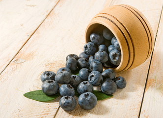 Blueberry berries scattered from a barrel on a wooden surface closeup.