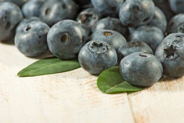 Group of blueberry berries with leaves on a wooden surface closeup.