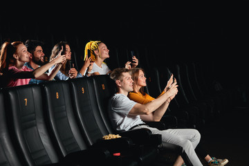 crazy funny men and women taking selfies in the dark cinema hall. side view photo