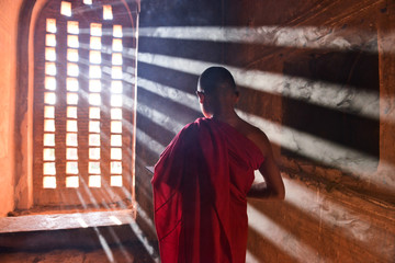 young buddhist novice monk dressed in red traditional robe praying in a buddhist temple wrapped in sunbeams