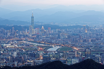 Night scenery of Downtown Taipei, the vibrant capital city of Taiwan, with view of  landmark Tower among high-rise buildings in Xinyi Financial District & bridges over Keelung River in blue twilight