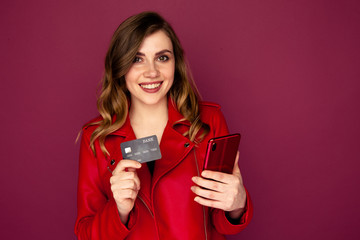 Happy young woman with credit card and cellphone standing in the studio.