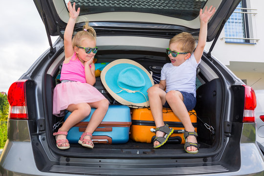 Twins boy and girl are sitting in the trunk of the car with luggage, ready to go for vacations.