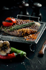 Grilled steak with knife and fork carved on black stone slate. Steak on a hot marble stone. Copy space, dark background, food fashion photo.
