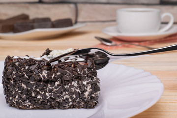 Dessert fork cuts off a piece of sponge cake with white cream and chocolate chips