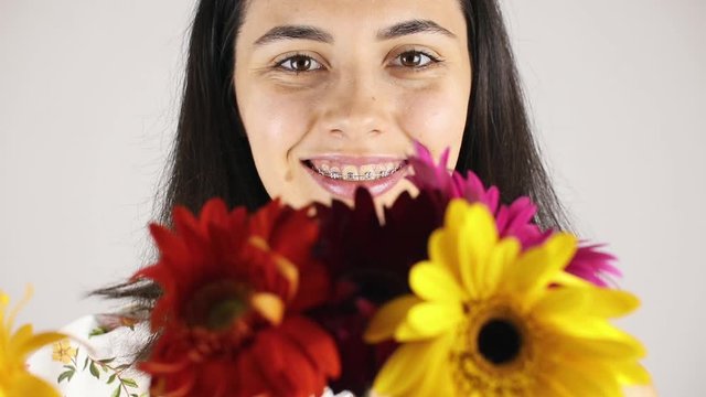 The girl face close up with a bouquet flowers. Portrait of a pretty young woman sniffing a bouquet flowers on grey background