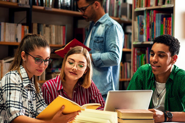 Four young students study in the school library, female student using laptop for researching online.