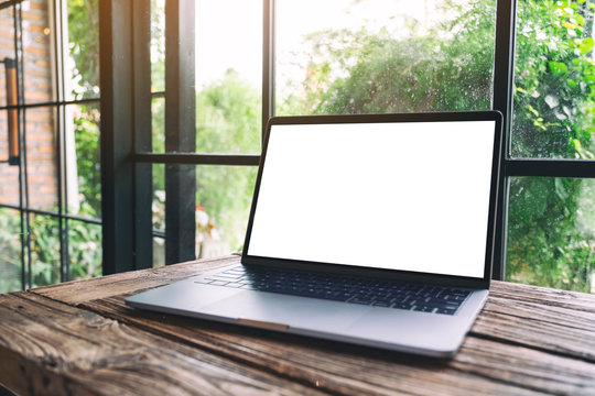 Mockup image of laptop computer with blank white desktop screen on wooden table