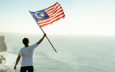 asian man with malaysia flag standing proudly on top of hill
