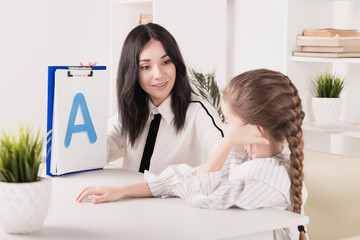 Child with therapist working on pronunciation and sounds together sitting in the class