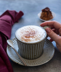 female hand holds a cup with cappuccino coffee on a gray background, close-up