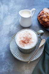 cappuccino coffee mug on saucer, milk and croissant on a gray background, copy space