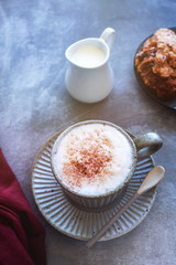 cappuccino coffee mug on saucer, milk and croissant on a gray background, copy space