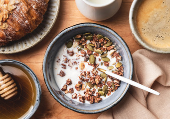 breakfast on a wooden table: granola, croissant, coffee and milk, top view, close-up