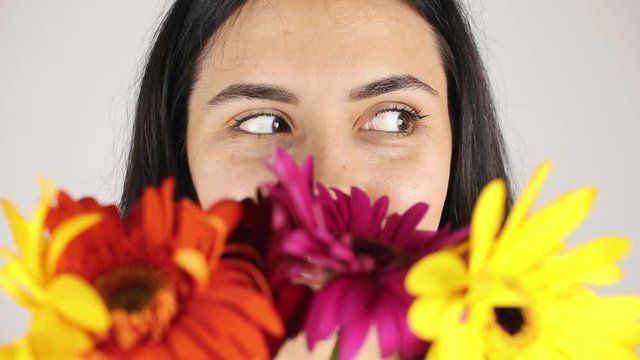 The girl face close up with a bouquet flowers. Portrait of a pretty young woman sniffing a bouquet flowers on grey background