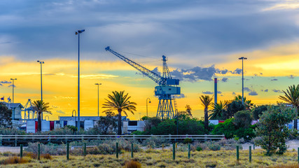 A vintage shipping crane against a yellow sunset sky