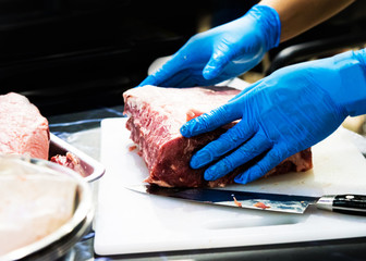 chef cuts raw meat with a knife on a board, Cook cuts raw meat