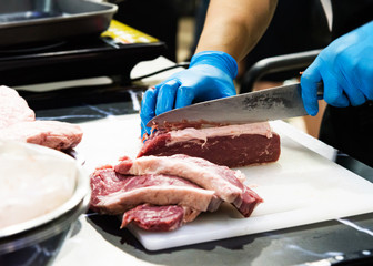 chef cuts raw meat with a knife on a board, Cook cuts raw meat