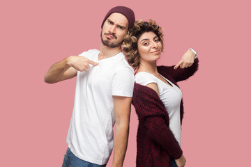 Portrait of satisfied successful couple of friends in casual style standing back to back, pointing...