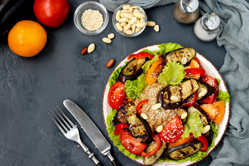 Salad with eggplant, tomato, paprika, lettuce, sesame and peanuts, top view on dark background, horizontal orientation