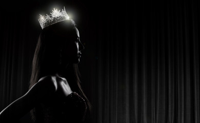 Portrait of Miss Pageant Beauty Contest in sequin Evening Ball Gown long dress with sparkle light Diamond Crown, silhouette low key exposure with curtain, studio lighting dark background dramatic © Jade