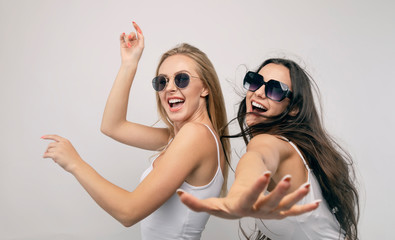Cheerful young women in white tank tops and sunglasses dancing isolated white background