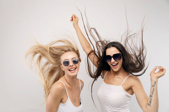 Two girls in white tank tops and sunglasses jumping with hair fluttering isolated white background