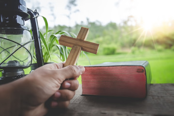 Christian holding wooden cross in hands with Bible on wooden table. religion concept.