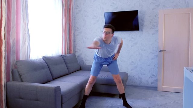 Funny nerd man in glasses is doing zumba exercises at home. Sport humor concept.