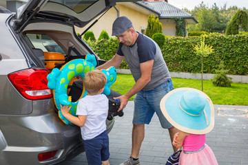 Father with little son and daughter are loading the car trunk with luggages for holidays