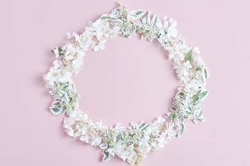 Nature floral round frame on pink background. ornament with white fresh hydrangea flowers, petals, and green leaves. flat lay, top view