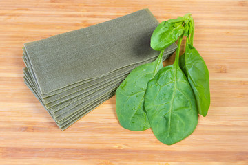 Uncooked green lasagna sheets and fresh spinach on cutting board