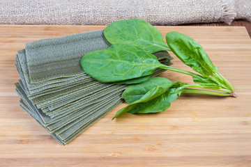 Uncooked green lasagna sheets and fresh spinach on cutting board