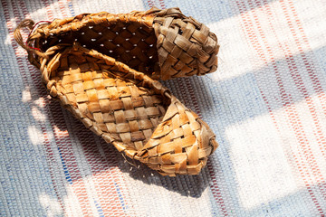 Birch bark shoes, traditional old Russian shoes lie on an old traditional carpet in the sun. Shoes...
