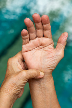 Trigger Finger, Senior woman's left hand massaging her right hand Suffering from pain, Close up and macro shot, Swimming pool background, Health care concept