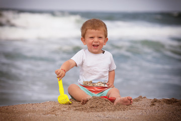 A cute little boy is sitting on the sea sand. Happy little boy on the beach. Summer. Recreation. Tourism.