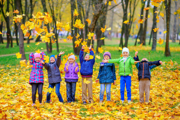 group of children playing in the autumn park, tossing up autumn foliage and having fun, outdoor...