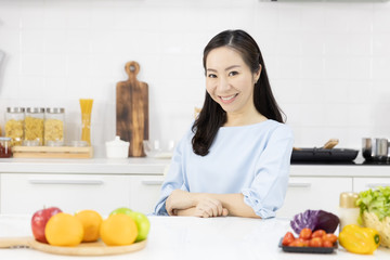 Portrait of Asian woman Smiling at you in the kitchen and salad ingredients on table at home. Healthy women and Healthy food concept