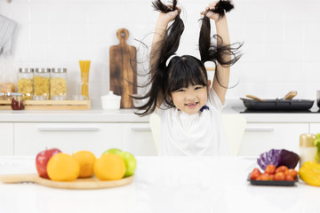Obraz na płótnie Canvas Portrait of Asian little girl Smiling at you in the kitchen and salad ingredients on table at home. Healthy food concept