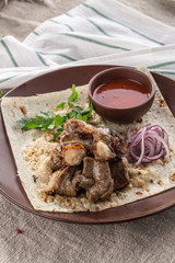 Shish kebab on lavash bread with red onion and tomato sauce on brown plate on tablecloth